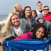 Students holding a GVSU flag by the ocean